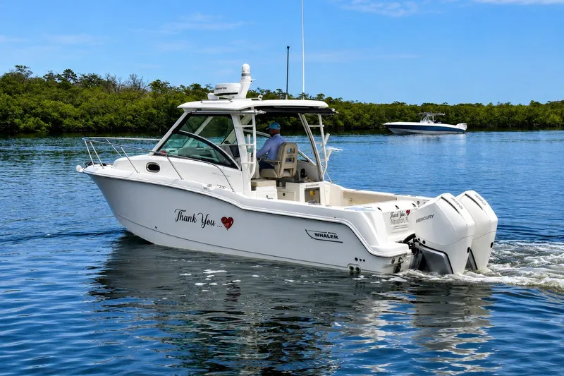 Slide: The Image of 2020 Boston Whaler 285 Conquest cruising on a serene lake with lush greenery. - 1