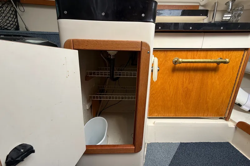Slide: The Image of 1998 Catalina 250 interior cabinet with open door, revealing shelves and plumbing. - 26