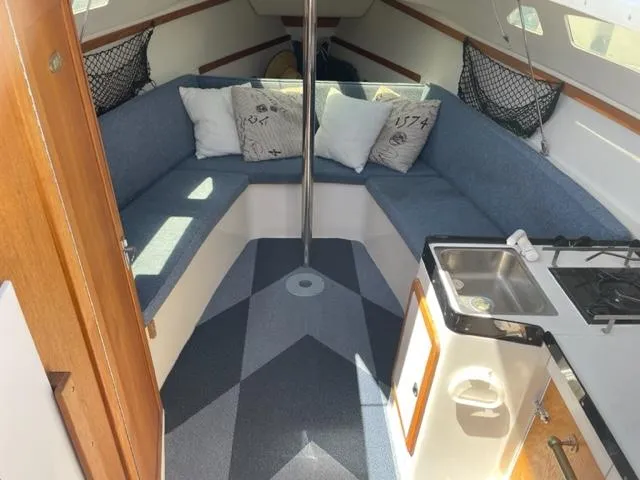 Slide: The Image of Interior of a 1998 Catalina 250 with blue seating cushions, pillows, and a small kitchenette. - 3