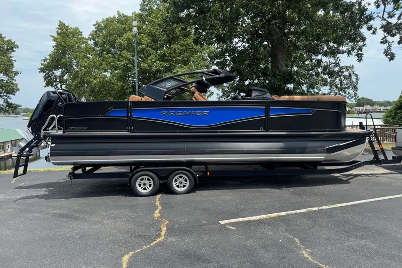 The Image of 2027 Premier 230 Intrigue RLO-DL pontoon boat on trailer, parked near a lake. - 1