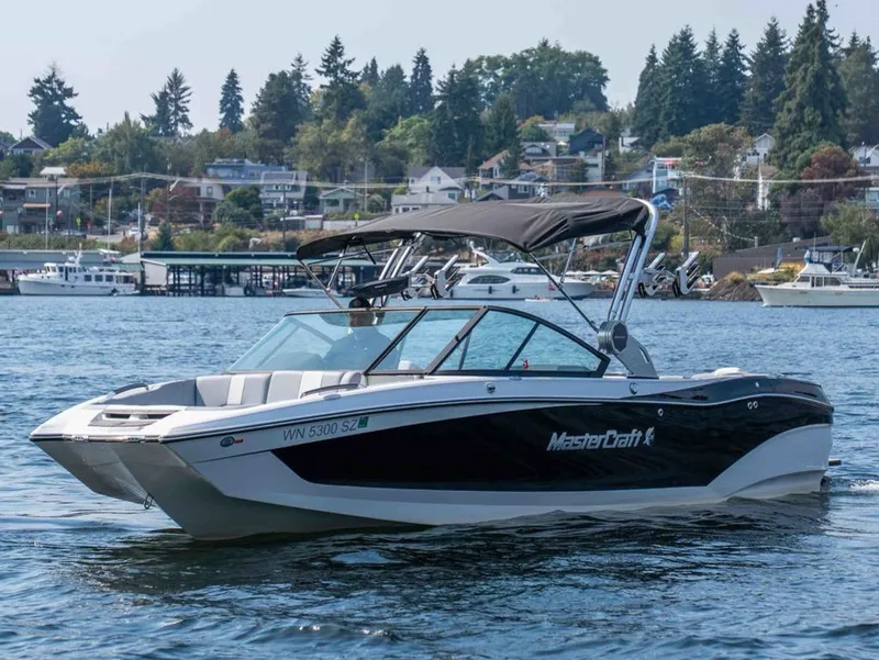 The Image of A 2022 MasterCraft X26 cruising on calm waters with wooded hills in the background. - 1