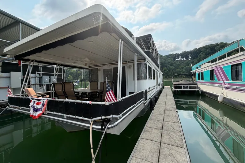 Slide: The Image of Houseboat docked at marina with American flags, featuring outdoor seating and scenic lake view. - 49