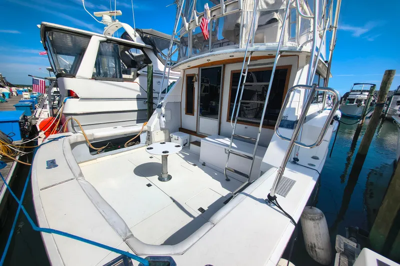 Slide: The Image of 1985 Bertram 42 Convertible yacht docked at marina, featuring spacious deck and ladder. - 2
