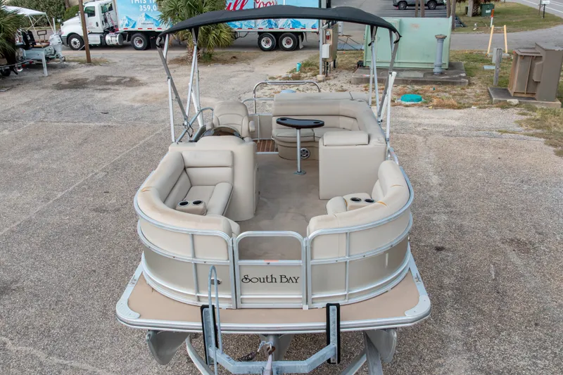 Slide: The Image of 2016 South Bay 5220CR pontoon boat with beige seating and canopy, parked on a trailer. - 1