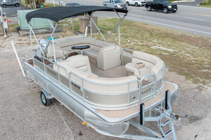 Slide: The Image of 2016 South Bay 5220CR pontoon boat on trailer, featuring beige seating and black canopy. - 5