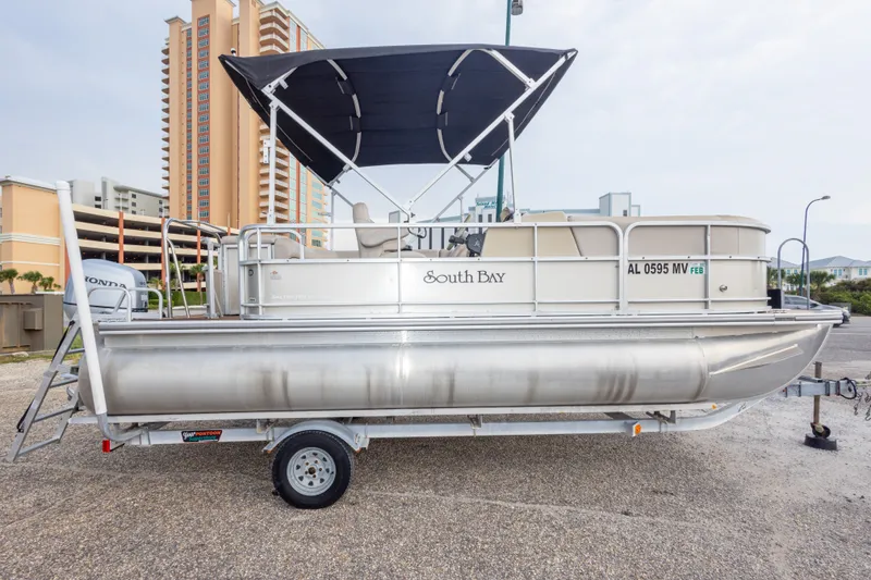 Slide: The Image of 2016 South Bay 5220CR pontoon boat with canopy on a trailer, parked near buildings. - 15