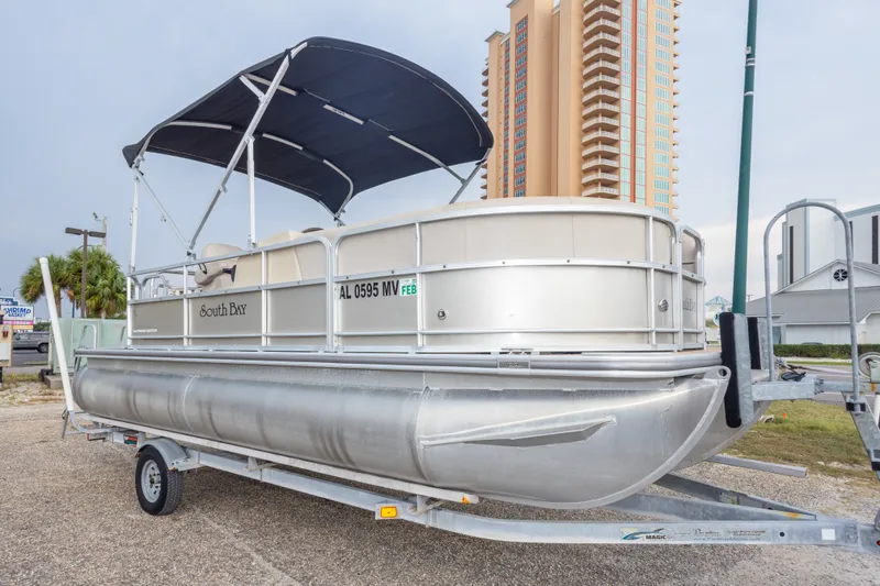 Slide: The Image of 2016 South Bay 5220CR pontoon boat on trailer, parked near tall buildings. - 16