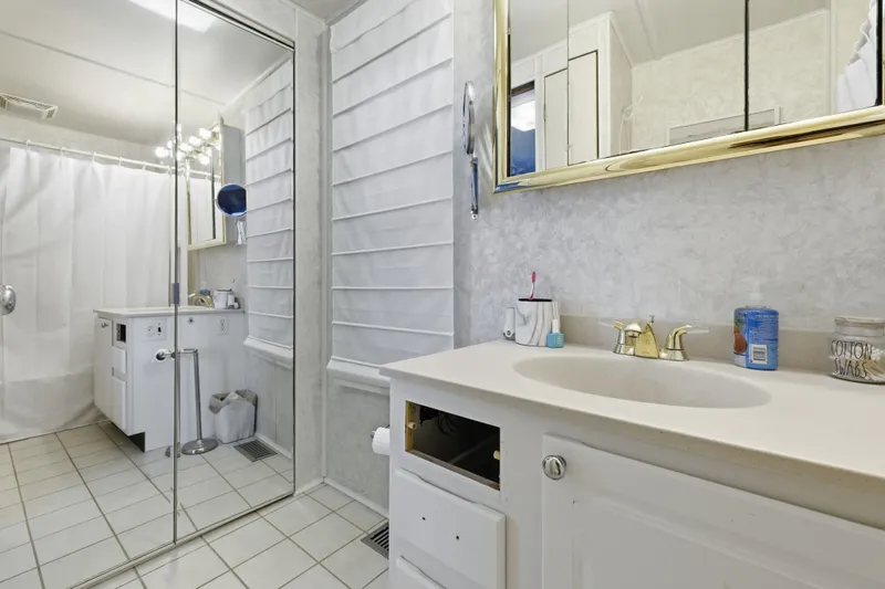 Slide: The Image of Bathroom with white tiles, mirrored cabinet, and gold faucet in a Monticello 16x70, 2002 model. - 62