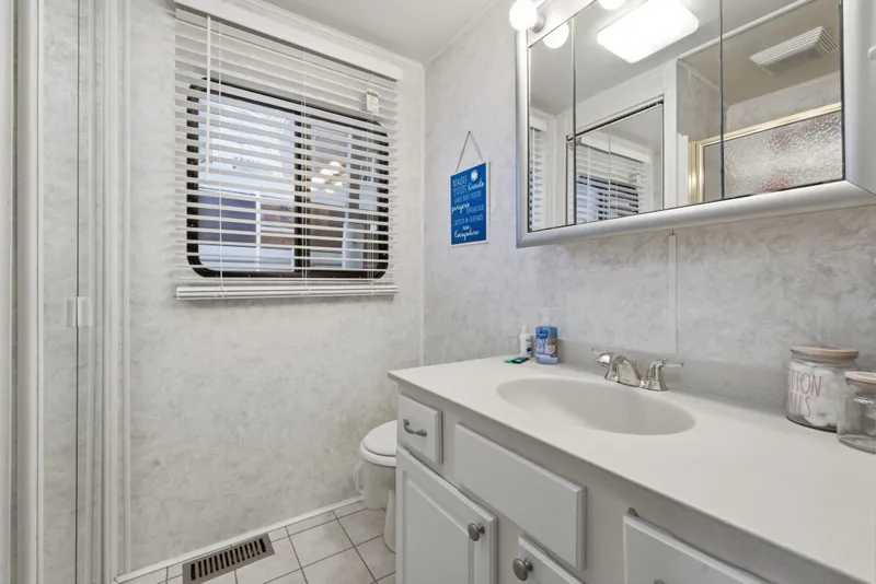 Slide: The Image of Compact bathroom with white cabinetry, mirror, and window blinds in a 2002 Monticello 16x70 model. - 45