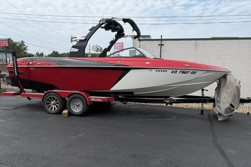 The Image of 2016 Malibu Wakesetter 25 LSV boat on trailer, red and white design, parked outdoors. - 0