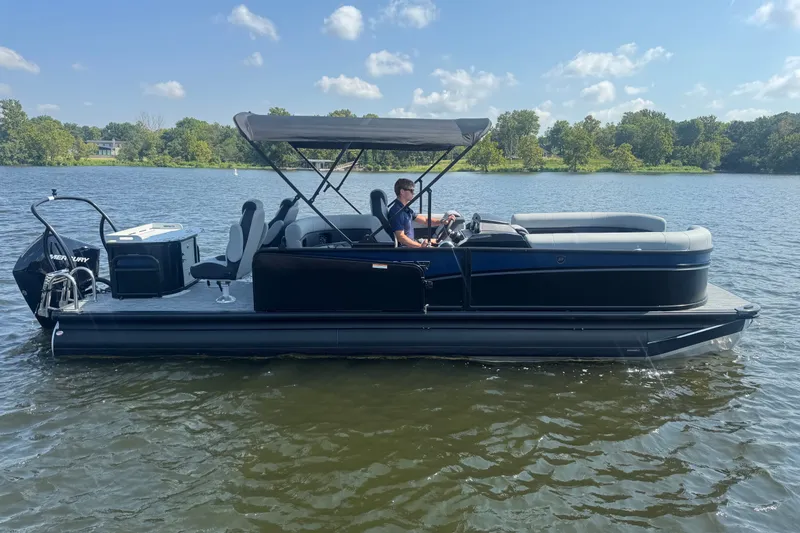 Slide: The Image of 2027 Premier 250 Sunsation pontoon boat cruising on a serene lake under a clear sky. - 2