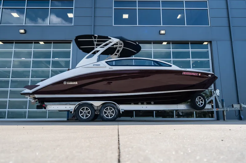 The Image of 2023 Yamaha Boats 275SE on trailer, parked outside modern building. - 1