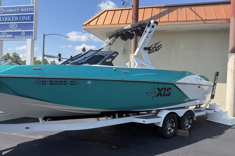 Slide: The Image of 2019 Axis A24 boat on trailer, teal and white, parked outside dealership. - 2