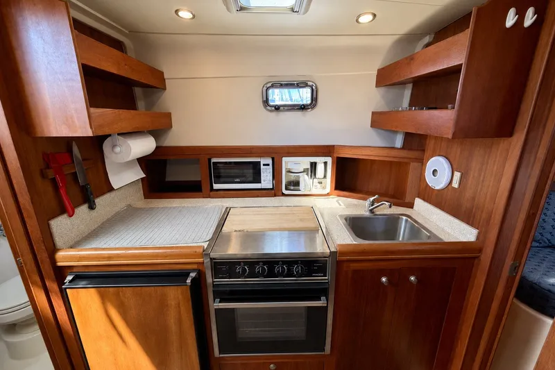 Slide: The Image of 2006 Mainship Pilot 34 Sedan galley with stove, sink, microwave, and wooden cabinetry. - 14