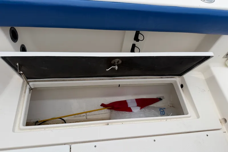 Slide: The Image of Open storage compartment on 2014 Robalo R305 Walkaround boat, containing a flag and ice bag. - 39