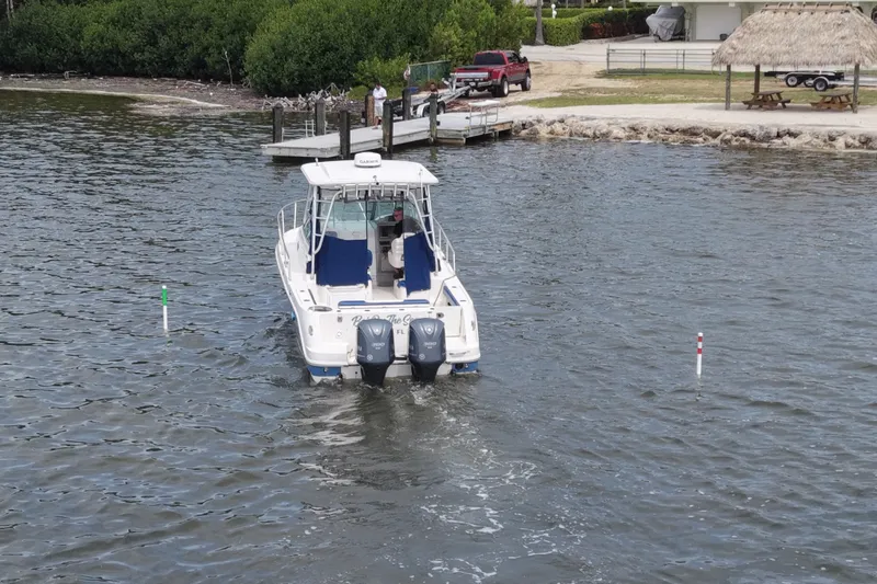 Slide: The Image of 2014 Robalo R305 Walkaround boat navigating near a dock with lush greenery. - 21