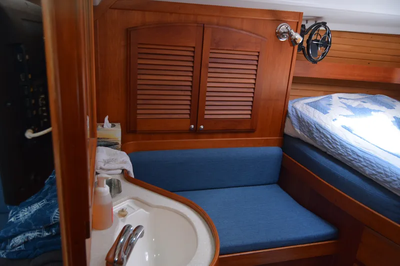 Slide: The Image of Cozy 2002 Sabre 402 yacht interior with wooden cabinetry, blue seating, and a compact sink area. - 89