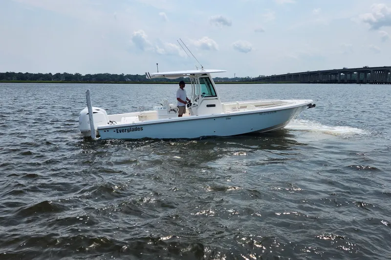 Slide: The Image of 2018 Everglades 273 Center Console boat cruising on a calm river near a bridge. - 15