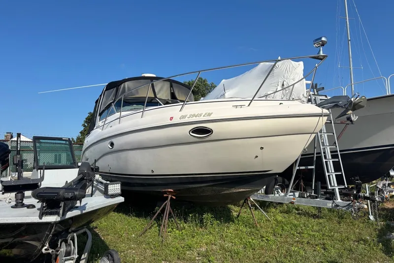 The Image of 2003 Rinker Fiesta Vee 312 boat on stands, parked outdoors under clear blue sky. - 0