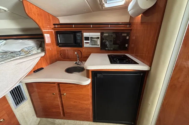 Slide: The Image of 2003 Rinker Fiesta Vee 312 boat interior with kitchenette, featuring sink, stove, and microwave. - 19