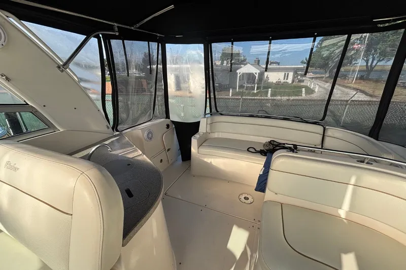 Slide: The Image of 2003 Rinker Fiesta Vee 312 boat interior with seating and helm, docked near a waterfront home. - 11