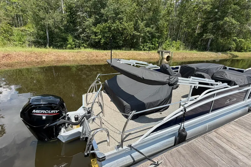 Slide: The Image of 2024 Barletta A22UC pontoon boat with Mercury engine docked by a wooded shoreline. - 4