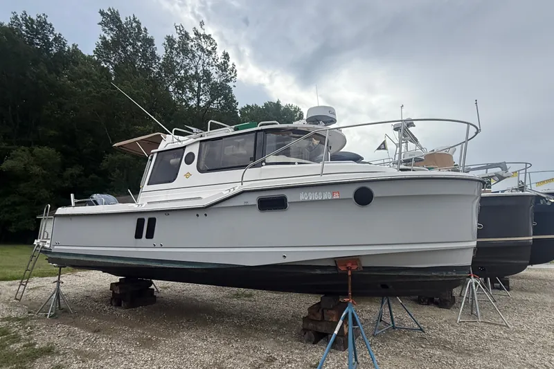 The Image of 2025 Ranger Tugs R-25 boat on stands, surrounded by trees and cloudy sky. - 0