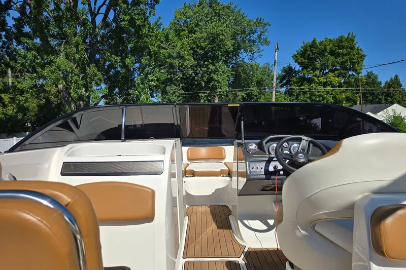 Slide: The Image of 2019 Bayliner VR6 Bowrider I/O interior with tan seating and steering wheel, surrounded by trees. - 6