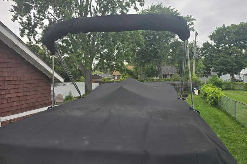 Slide: The Image of 2019 Bayliner VR6 Bowrider I/O with black cover and bimini top in a backyard setting. - 18