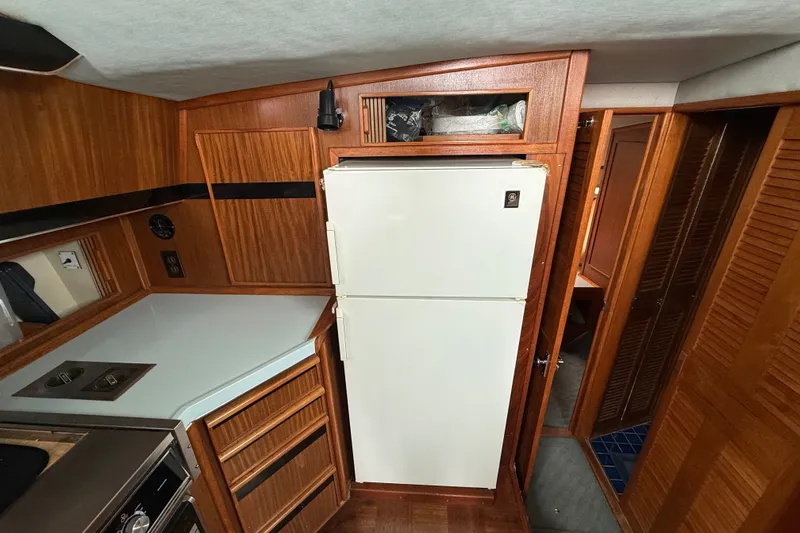 Slide: The Image of 1987 Sea Ray 410 Aft Cabin kitchen with wooden cabinetry and white refrigerator. - 18