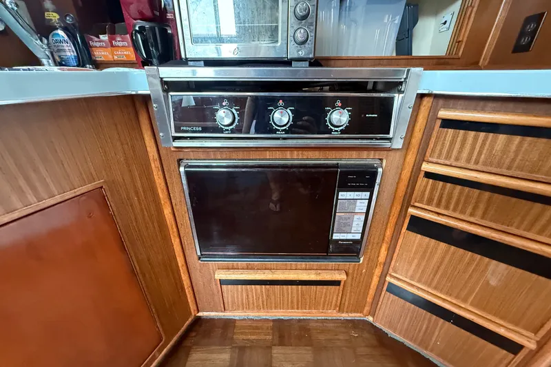 Slide: The Image of 1987 Sea Ray 410 Aft Cabin kitchen with stove and microwave, featuring wooden cabinetry. - 17