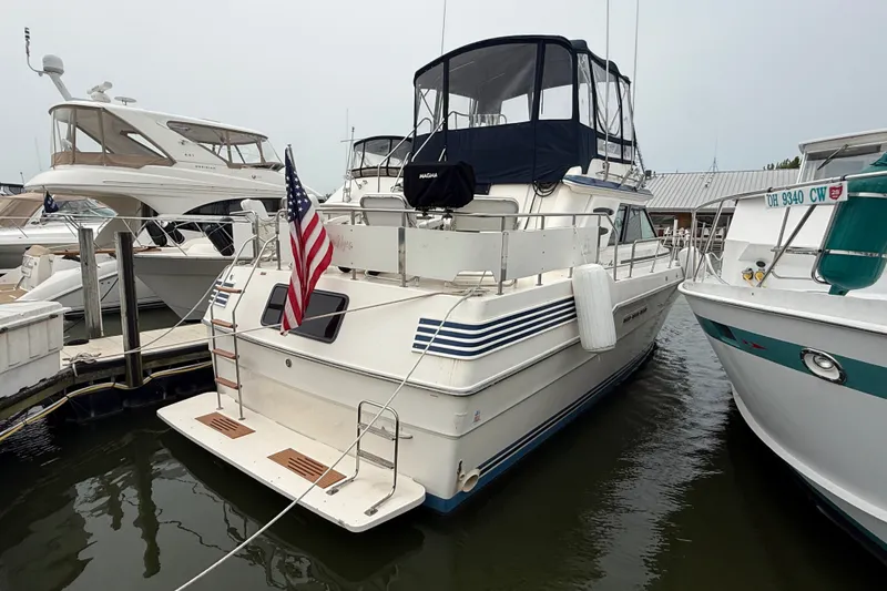 Slide: The Image of 1987 Sea Ray 410 Aft Cabin yacht docked, featuring American flag and enclosed flybridge. - 1