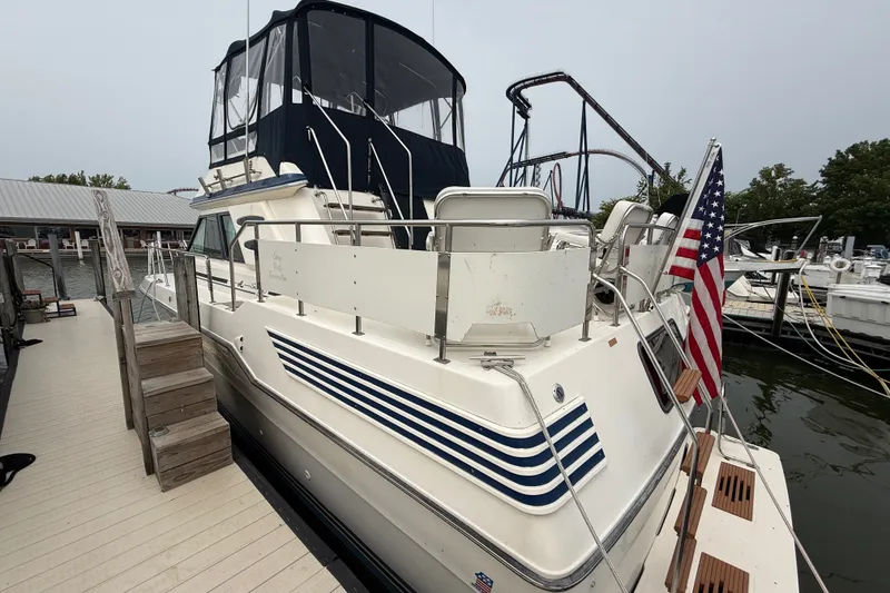 Slide: The Image of 1987 Sea Ray 410 Aft Cabin yacht docked, featuring American flag and blue-striped design. - 3