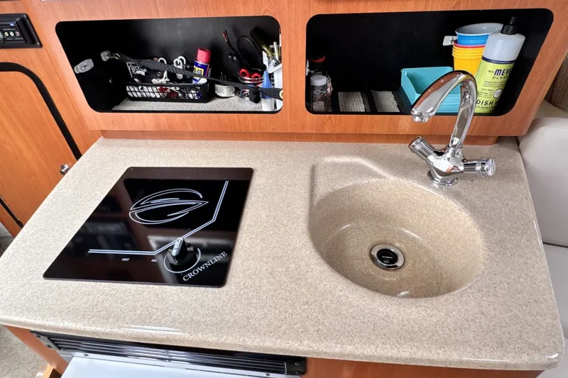 Slide: The Image of Crownline 280 CRX 2010 boat kitchenette with sink and stove, organized storage shelves. - 13