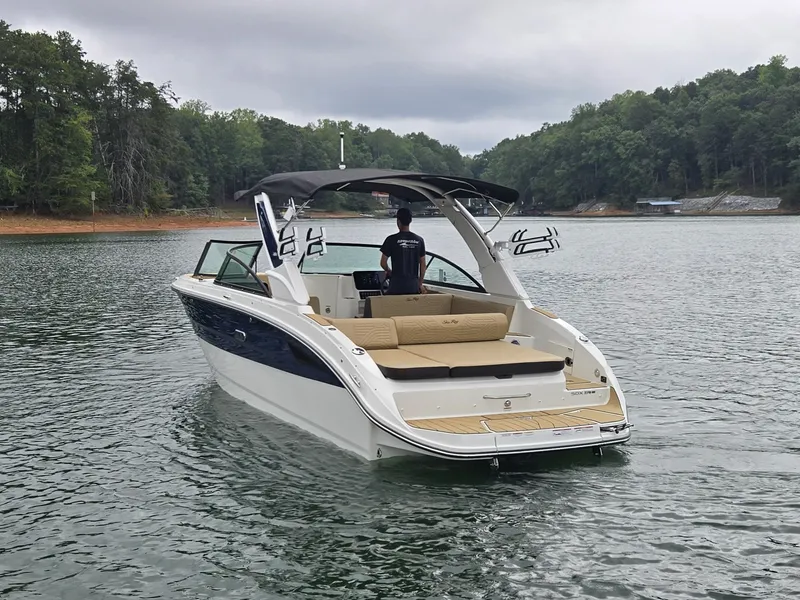 Slide: The Image of A 2027 Sea Ray SDX 270 Surf on a calm lake. It features sleek design with a black bimini top and beige seating. - 29