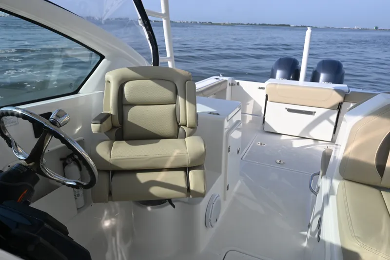 Slide: The Image of 2021 Pursuit DC 266 Dual Console boat interior with steering wheel and seating, on calm water. - 18