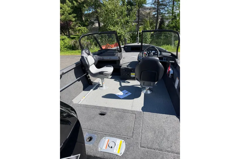 Slide: The Image of 2026 Crestliner 1750 Hawk WT boat interior with seating and dashboard, surrounded by greenery. - 21