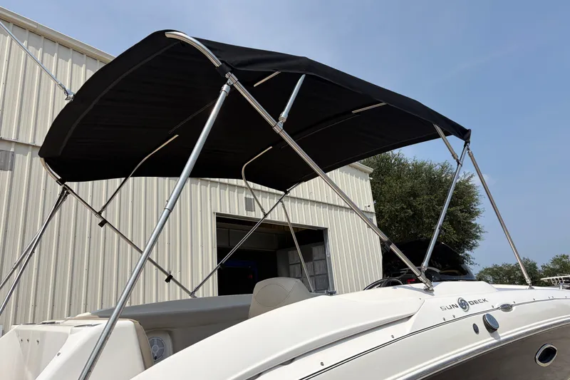 Slide: The Image of 2012 Hurricane SunDeck Sport 220 OB boat with black canopy, parked near a metal building. - 17