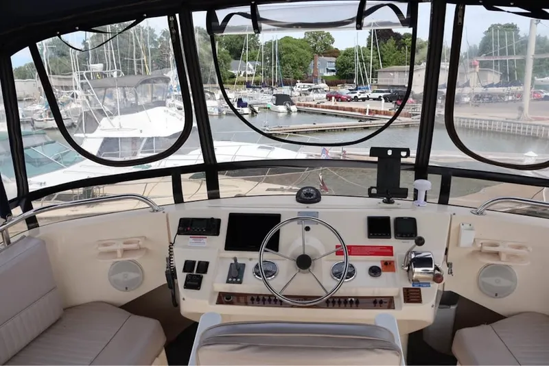 Slide: The Image of 2004 Mainship 390 Trawler helm with marina view, featuring steering wheel and navigation controls. - 1