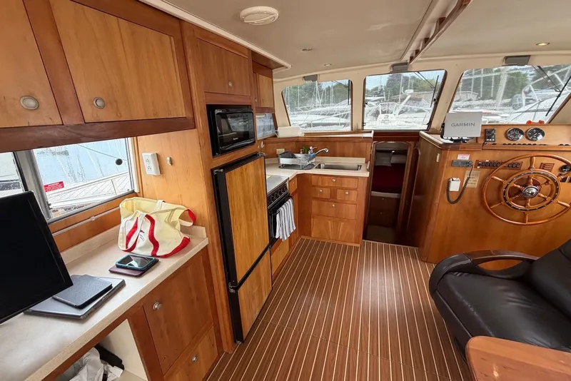 Slide: The Image of 2004 Mainship 390 Trawler interior with wooden cabinetry, helm, and kitchen area. - 16
