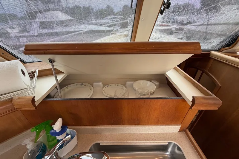 Slide: The Image of 2004 Mainship 390 Trawler kitchen with open cabinet, dishes, and cleaning supplies. - 19