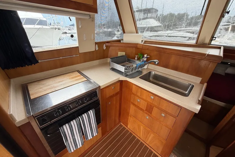 Slide: The Image of 2004 Mainship 390 Trawler kitchen with stove, sink, and wooden cabinetry. - 17