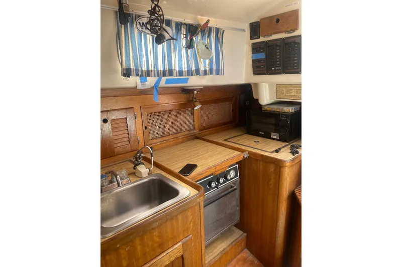 Slide: The Image of 1982 Bristol 40 yacht kitchen with wooden cabinetry, sink, oven, and striped curtains. - 2