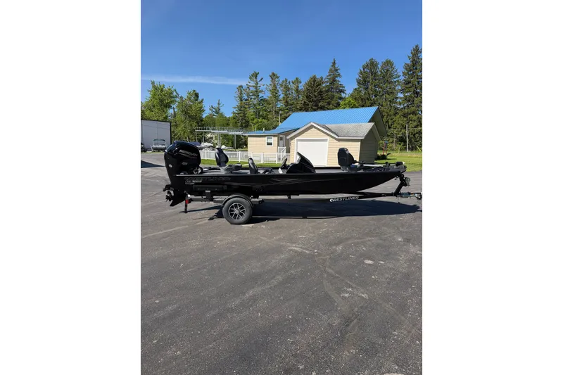 Slide: The Image of 2026 Crestliner XFC 179 fishing boat on trailer, parked outdoors with trees and building in background. - 6