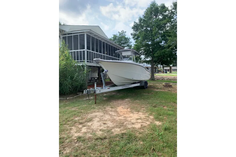 Slide: The Image of 2005 Triton 2895 CC boat on trailer beside a house, surrounded by greenery. - 1