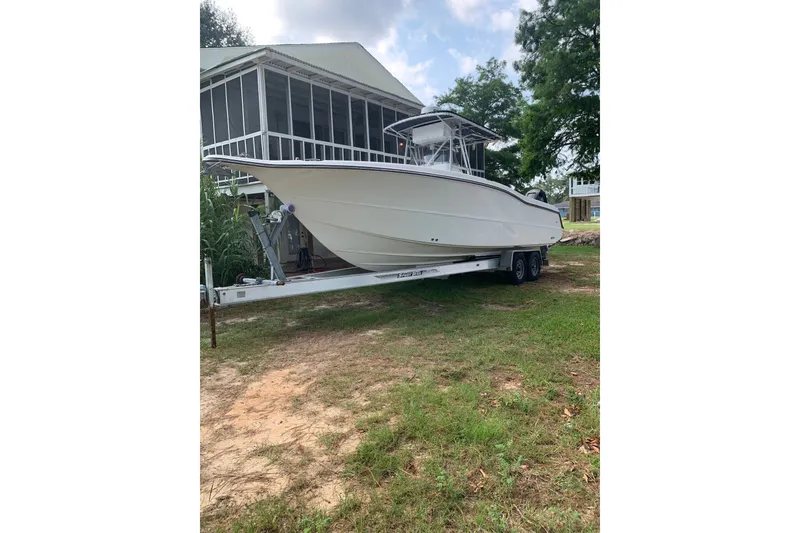 The Image of 2005 Triton 2895 CC boat on trailer, parked near a house with greenery. - 0