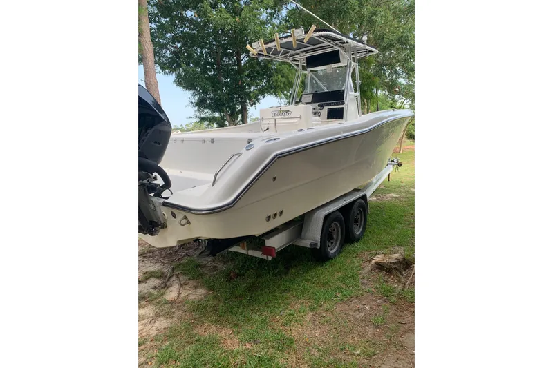 Slide: The Image of 2005 Triton 2895 CC boat on trailer, parked on grass with trees in background. - 4