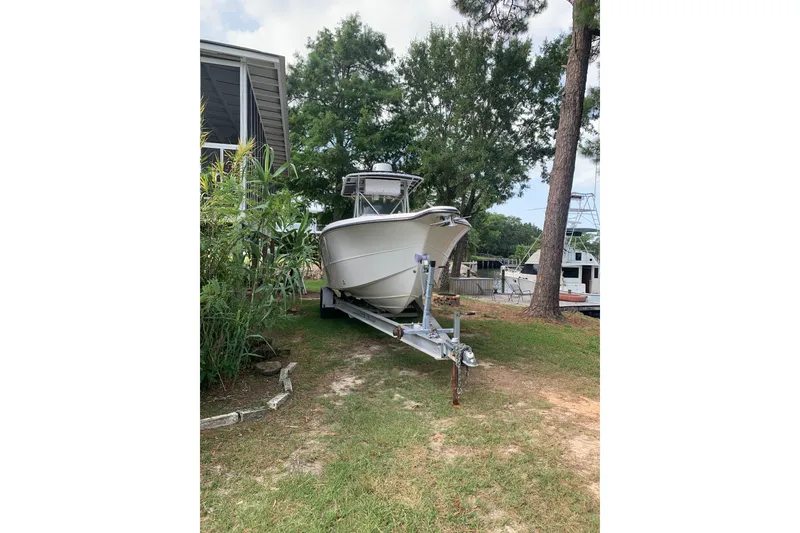 Slide: The Image of 2005 Triton 2895 CC boat on trailer, parked near trees and a house. - 5