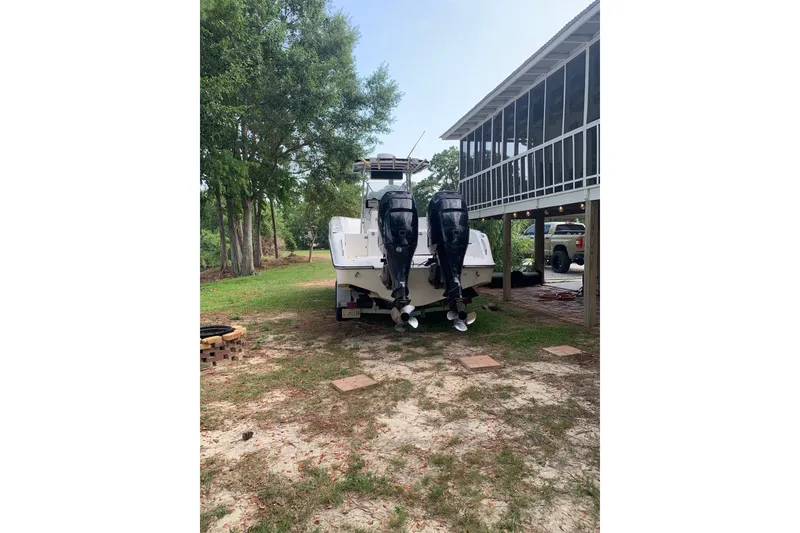 Slide: The Image of 2005 Triton 2895 CC boat with dual outboard motors parked near a house. - 2