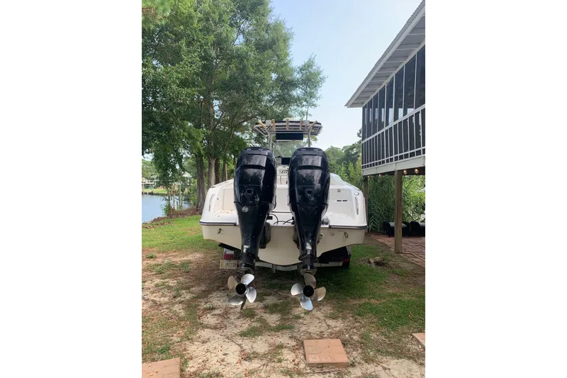 Slide: The Image of 2005 Triton 2895 CC boat with dual outboard motors, parked near a lakeside house. - 3